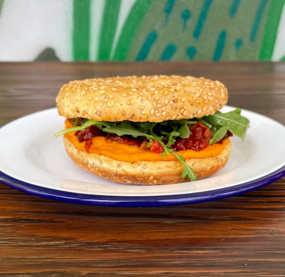 Bagel de hummus de pimiento rojo casero con tomates secos y rucula